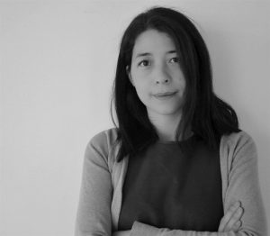 A black and white picture of Akiko, who has straight black hair and is wearing a light coloured cardigan over a tshirt