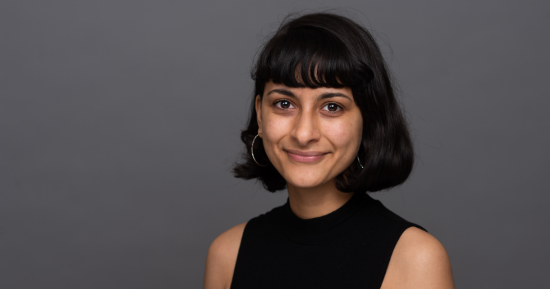 a photograph of Mary, NSUN Policy Officer, smiling at the camera against a dark grey background. She has short black hair with a fringe and is wearing a black tshirt.