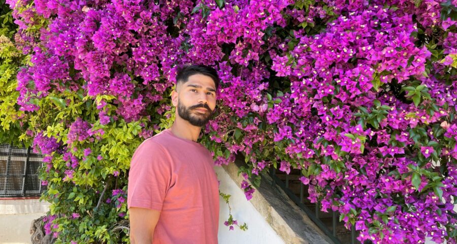 Photo of Taimour standing in front of purple flowers in a peach colour tshirt