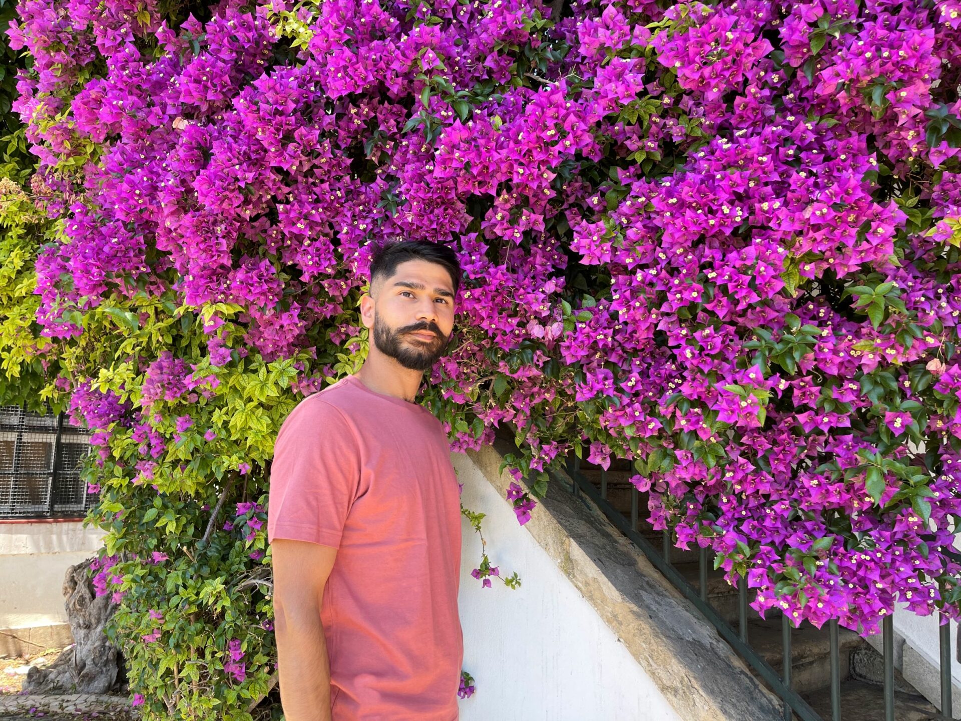 Photo of Taimour standing in front of purple flowers in a peach colour tshirt