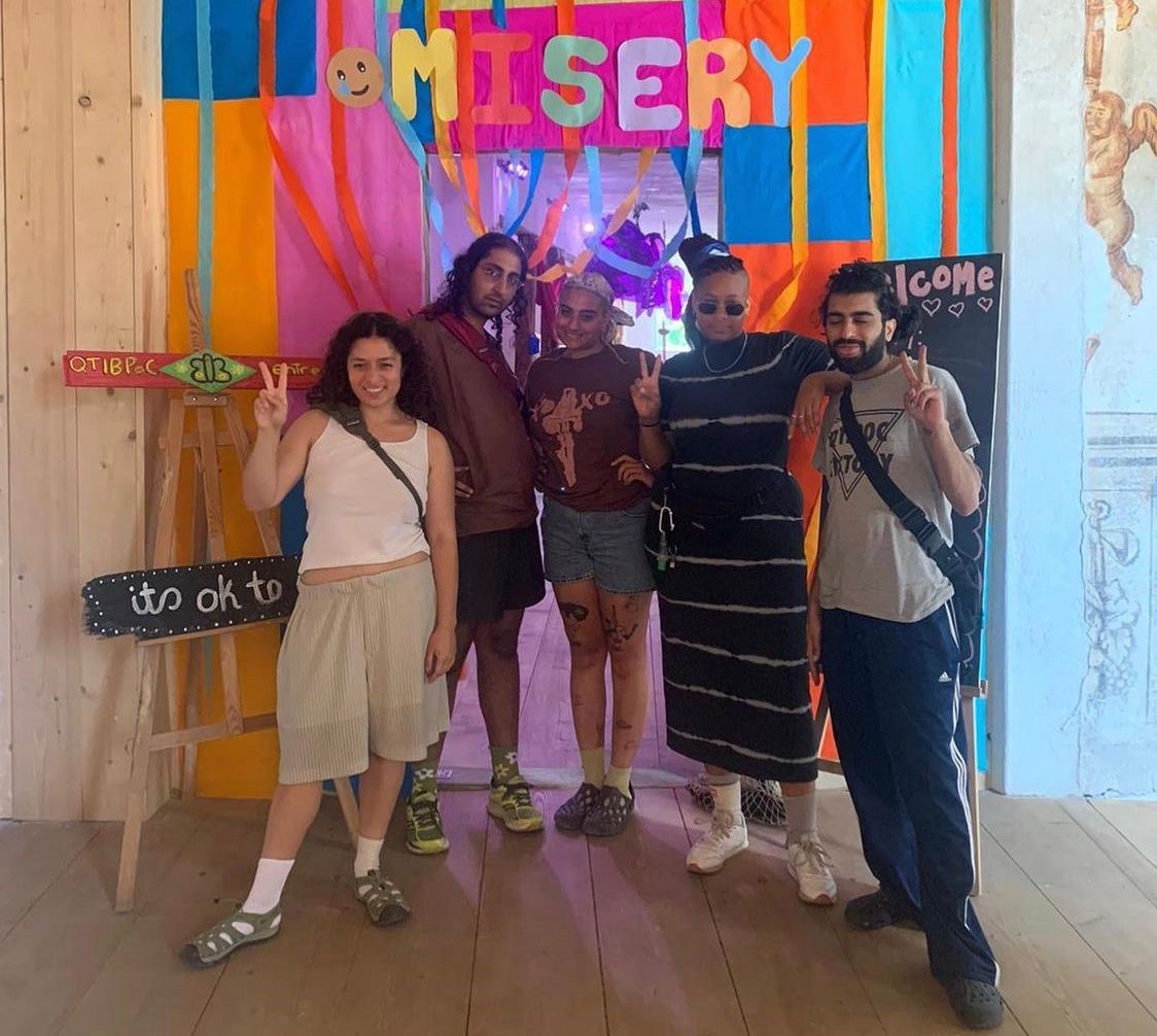 A group photograph of some of the members of misery standing in front of a colourful background with the word 'misery' above them