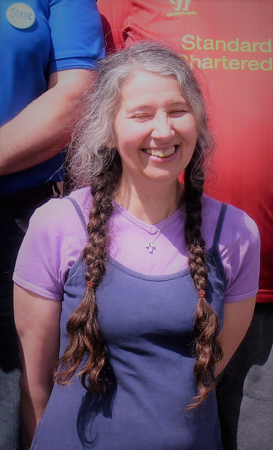 A picture of Clare, who is wearing a blue dress over a purple t-shirt, and is standing in a group of people