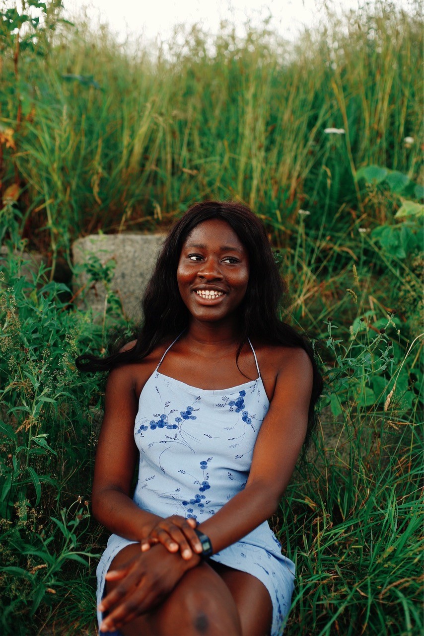 A photo of Nkechi, who is wearing a blue dress, sat amongst some greenery