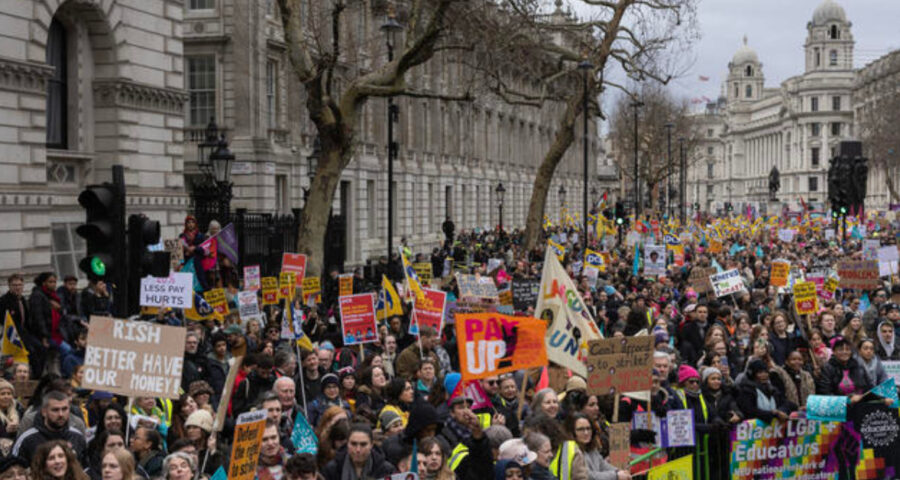 A photograph of strikers and protesters holding signs and placards on a street in London