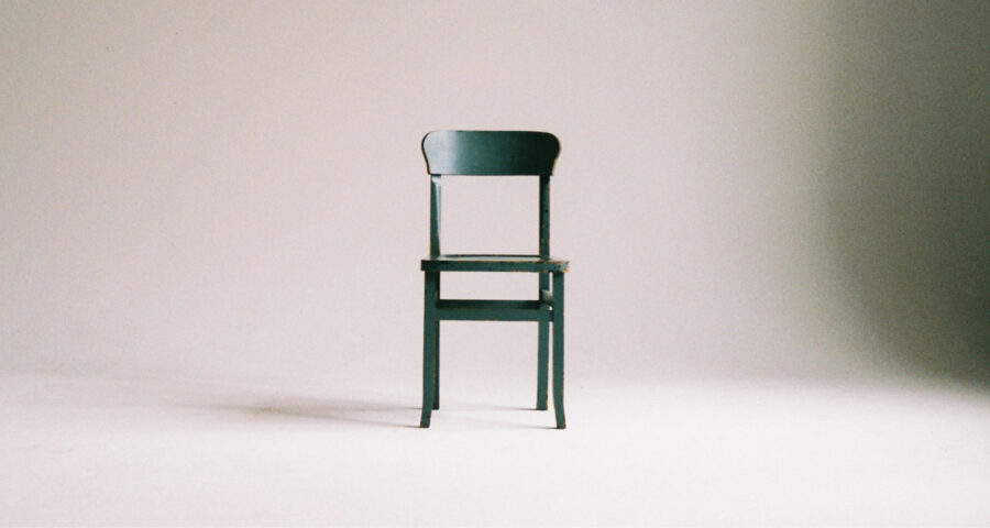 A dark green wooden chair sits in the middle of an empty space
