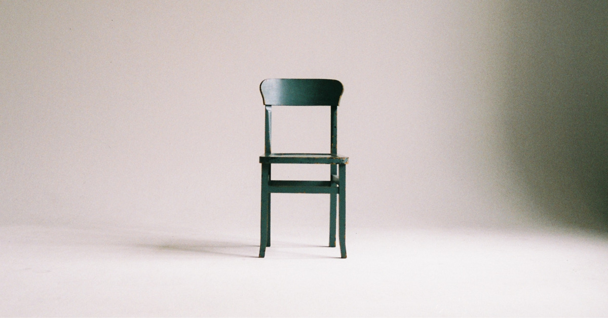 A dark green wooden chair sits in the middle of an empty space